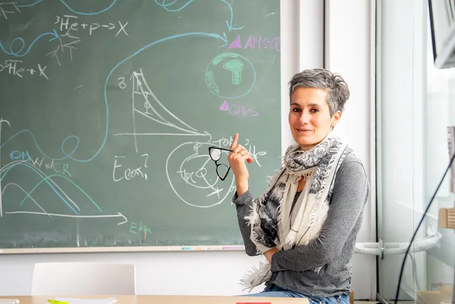 Color photo of a person holding reading glasses leaning against a wall