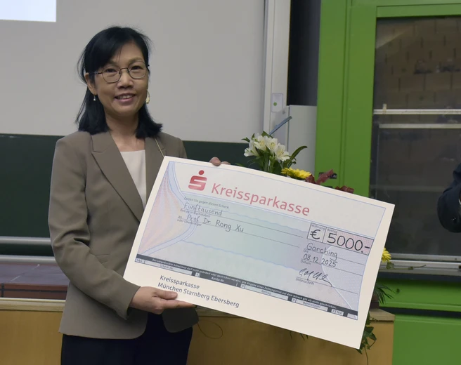 Color photo of a person smiling and holding a large format "check" for an award