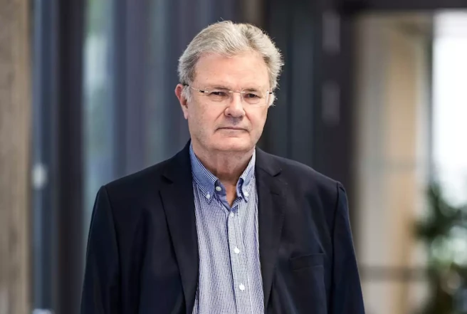 Color photo of a person facing the camera wearing a blue shirt and dark jacket