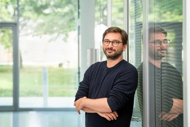 Color foto of a person wearing glasses leaning up against a wall