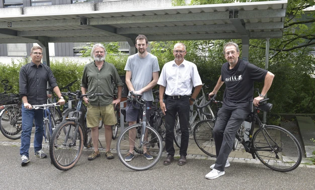 Color photo of 5 people standing outside with bicycles