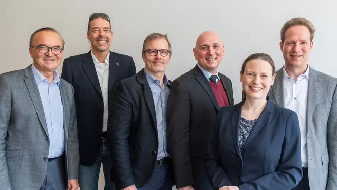 Six people wearing suit jackets smile at the camera