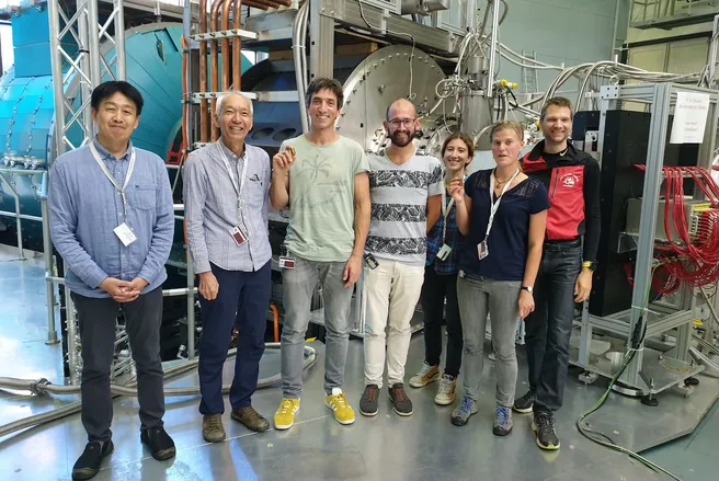 Color photo of seven people smiling and standing in front of scientific equipment