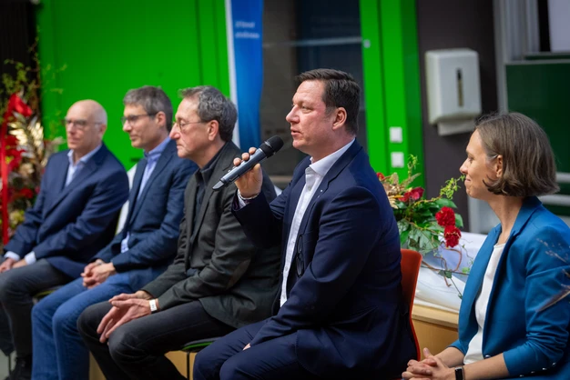 Color photo of five people presenting with a microphone
