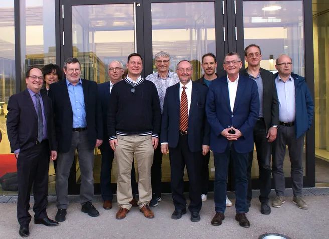 Color photo of 11 people standing in front of a building smiling all wearing suits